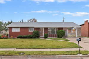 Ranch-style home with a front yard, concrete driveway, a carport, and a shingled roof