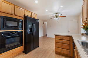 Kitchen featuring black appliances, a peninsula, light countertops, light wood-type flooring, and recessed lighting