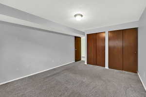 Unfurnished bedroom featuring a textured ceiling, multiple closets, and carpet