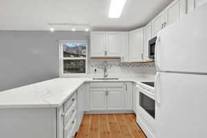 Kitchen with white appliances, a peninsula, light wood-type flooring, rail lighting, and white cabinets