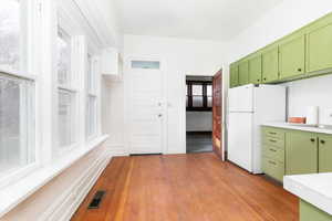 Kitchen featuring green cabinets, light countertops, freestanding refrigerator, and light wood-type flooring