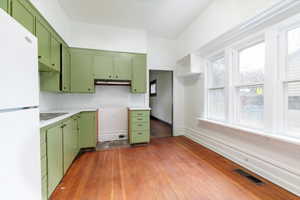 Kitchen featuring green cabinetry, freestanding refrigerator, light countertops, dark wood finished floors, and decorative backsplash