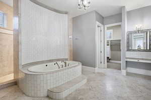 Bathroom featuring a spacious closet, vanity, a garden tub, a chandelier, and walk in shower