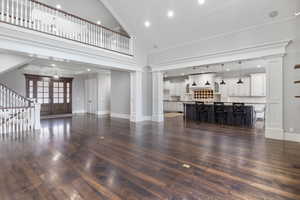 Unfurnished living room with stairway, ornate columns, high vaulted ceiling, dark wood-style flooring, and recessed lighting