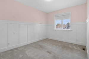 Spare room featuring a wainscoted wall, a decorative wall, and light carpet