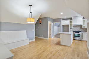 Kitchen with stainless steel range oven, white cabinets, glass insert cabinets, light wood-style floors, and recessed lighting