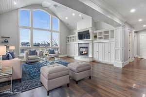 Living room featuring dark wood-style flooring, a glass covered fireplace, high vaulted ceiling, and recessed lighting