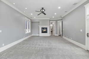Unfurnished living room with a glass covered fireplace, recessed lighting, ornamental molding, a ceiling fan, and light carpet