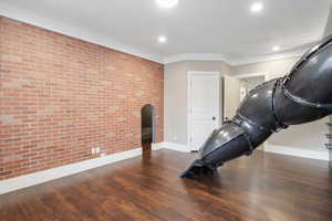 Exercise area with brick wall, dark wood-type flooring, arched walkways, recessed lighting, and an accent wall