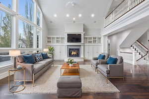 Living area featuring high vaulted ceiling, wood finished floors, a warm lit fireplace, plenty of natural light, and stairs