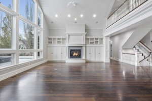 Unfurnished living room featuring high vaulted ceiling, a lit fireplace, dark wood-style floors, stairs, and wooden ceiling