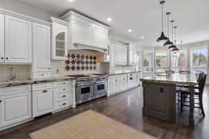 Kitchen featuring dark stone countertops, double oven range, white cabinets, a kitchen bar, and a kitchen island with sink