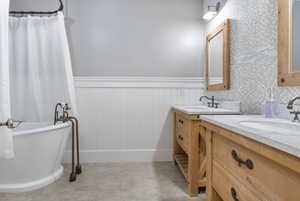 Full bathroom with wainscoting, two vanities, a tub to relax in, light floors, and curtained shower