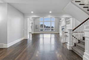 Unfurnished living room with stairway, crown molding, dark wood-style floors, a fireplace, and recessed lighting