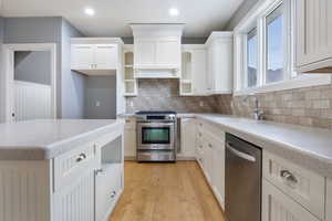 Kitchen with white cabinetry, appliances with stainless steel finishes, open shelves, light stone countertops, and light wood-type flooring