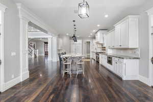 Kitchen featuring ornate columns, a kitchen breakfast bar, decorative light fixtures, backsplash, and light stone countertops