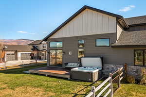 Rear view of property with board and batten siding, a shingled roof, stone siding, a deck with mountain view, and a hot tub