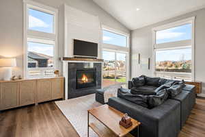 Living room featuring dark wood-type flooring, a high end fireplace, high vaulted ceiling, and recessed lighting