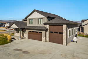 View of front facade with driveway, stone siding, a shingled roof, and board and batten siding