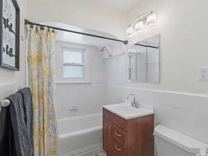 Bathroom with vanity, shower / bath combination with curtain, tile walls, and wainscoting