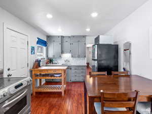 Kitchen with gray cabinetry, stainless steel appliances, light countertops, dark wood-type flooring, and decorative backsplash