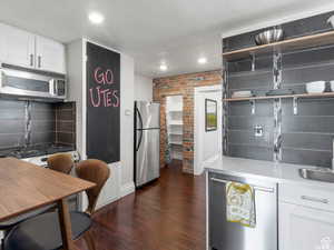 Kitchen with white cabinets, open shelves, appliances with stainless steel finishes, dark wood-style flooring, and recessed lighting