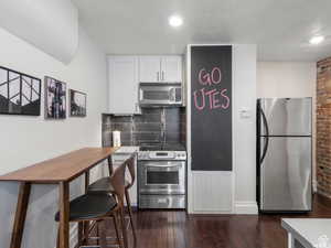 Kitchen featuring appliances with stainless steel finishes, white cabinets, dark wood finished floors, backsplash, and a textured ceiling