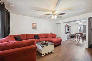 Living room featuring wood finished floors, ornamental molding, a textured ceiling, and ceiling fan