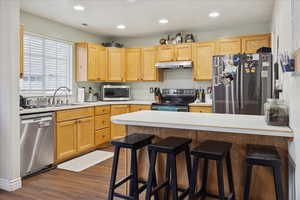 Kitchen with stainless steel appliances, light countertops, a breakfast bar area, dark wood-style flooring, and a peninsula