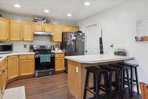Kitchen with appliances with stainless steel finishes, a breakfast bar, light countertops, dark wood finished floors, and recessed lighting