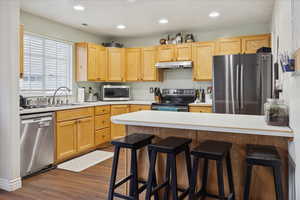 Kitchen featuring appliances with stainless steel finishes, light countertops, a kitchen bar, dark wood-type flooring, and a peninsula