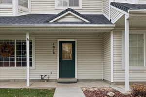 Doorway to property featuring roof with shingles and covered porch