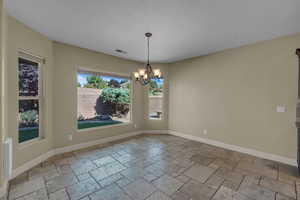 Unfurnished dining area featuring a chandelier and stone tile flooring