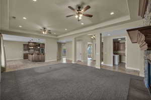 Unfurnished living room with ceiling fan, a raised ceiling, a fireplace, arched walkways, and recessed lighting