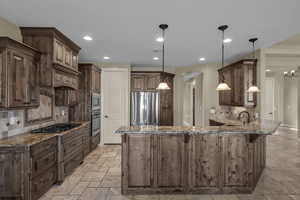 Kitchen with backsplash, stone tile flooring, dark stone counters, a peninsula, and decorative light fixtures