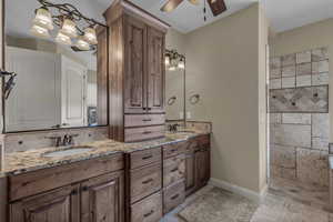 Bathroom featuring double vanity, a ceiling fan, and stone tile flooring