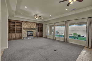 Unfurnished living room with a ceiling fan, a raised ceiling, recessed lighting, a stone fireplace, and light carpet