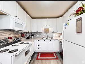 Kitchen featuring white appliances, light countertops, white cabinets, dark wood-style floors, and tasteful backsplash