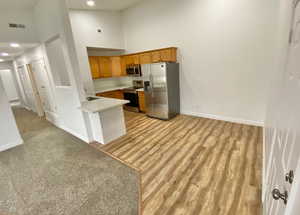 Kitchen featuring stainless steel appliances, high vaulted ceiling, brown cabinetry, light wood-type flooring, and backsplash