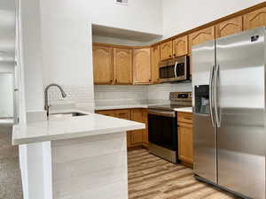 Kitchen with stainless steel appliances, light stone countertops, light wood finished floors, a peninsula, and backsplash