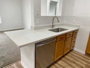 Kitchen featuring stainless steel dishwasher, light stone counters, brown cabinets, tasteful backsplash, and light wood-style flooring