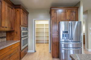 Kitchen with appliances with stainless steel finishes, brown cabinets, light wood-style floors, and decorative backsplash