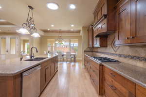 Kitchen with hanging light fixtures, dark stone counters, brown cabinets, stainless steel appliances, and recessed lighting
