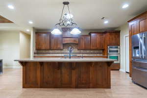 Kitchen featuring a kitchen bar, stainless steel appliances, tasteful backsplash, decorative light fixtures, and a kitchen island with sink