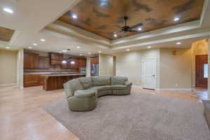 Living room with light wood-style floors, a raised ceiling, and a ceiling fan