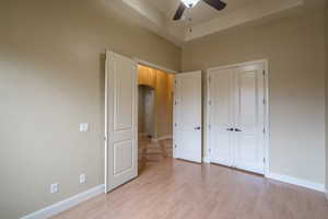 Unfurnished bedroom with a tray ceiling, arched walkways, light wood finished floors, a ceiling fan, and a closet