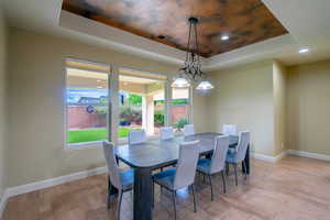 Dining space with a raised ceiling, light wood finished floors, and recessed lighting