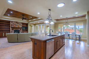 Kitchen featuring decorative light fixtures, light stone counters, light wood-type flooring, a fireplace, and dishwasher