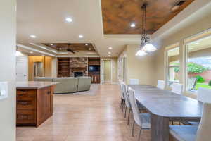 Dining room featuring a stone fireplace, a tray ceiling, a ceiling fan, recessed lighting, and built in shelves