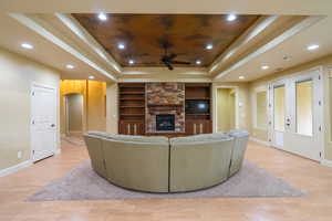 Living area with a raised ceiling, built in features, french doors, arched walkways, and light wood-style floors